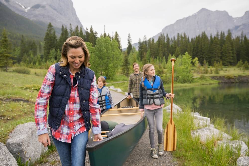 A family carrying a canoe by a lake.