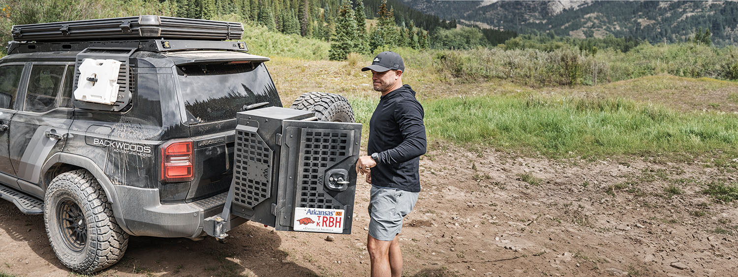 A man using the backwoods adventure mods rear storage box in the back of a land cruiser 250 series.
