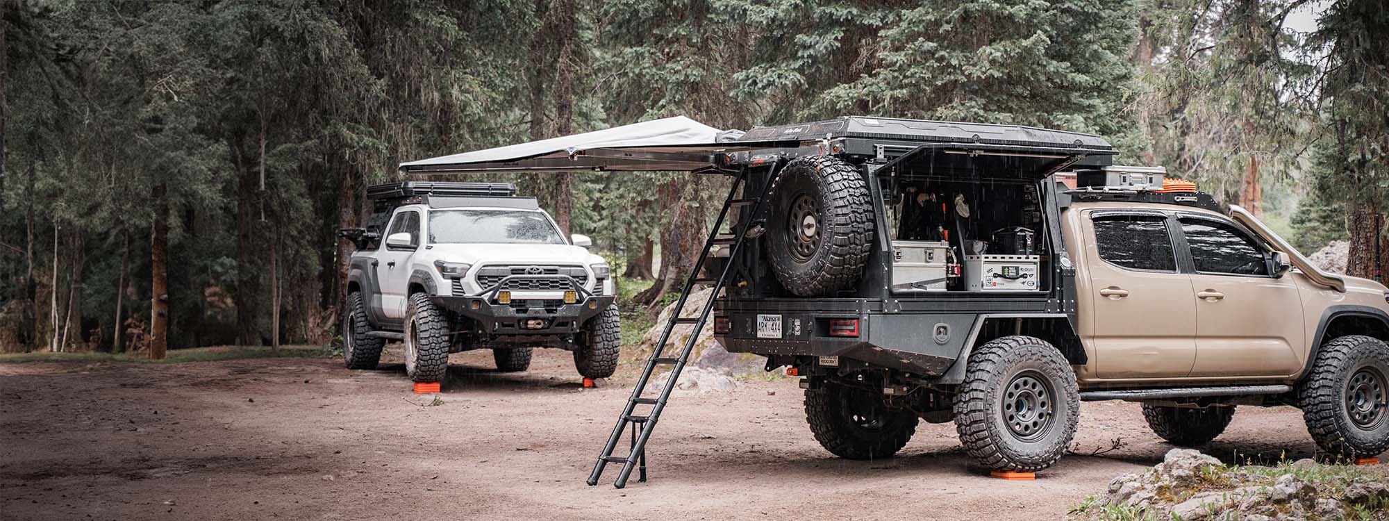 Two Toyota Tacoma trucks set up for camping and overlanding with several off road accessories installed