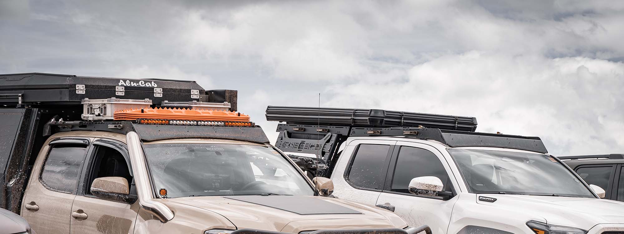 two Toyota Tacomas with roof racks installed carrying overland storage boxes and off road recovery gear