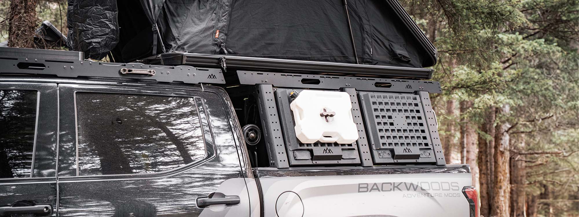 A 3rd gen Toyota Tundra truck with a backwoods adventure mods bed rack and roof rack in the woods camping.