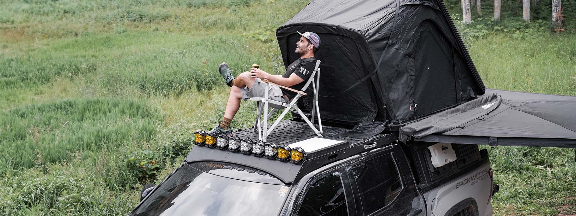 A man sitting on a Backwoods Adventure Mods Toyota Tundra DRIFTR Roof Rack looking at the sunset.