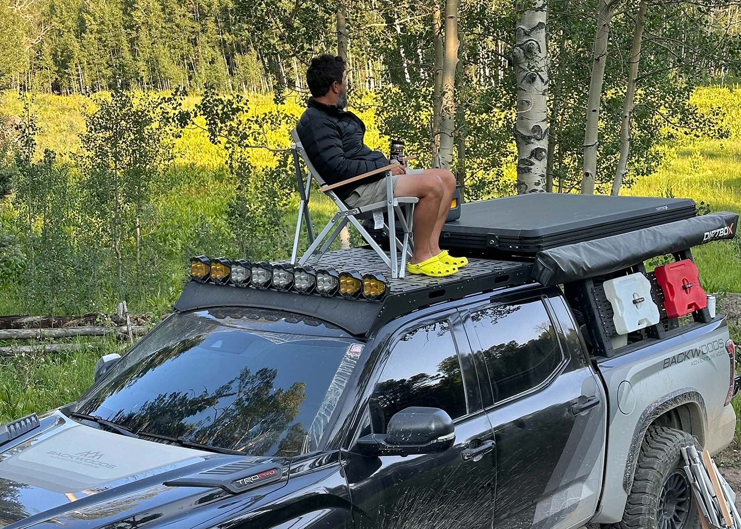 Man relaxing in a camp chair on top of his 3rd Gen Toyota Tundra with a Backwoods Adventure Mods DRIFTR roof rack installed with optional deck plate accessories