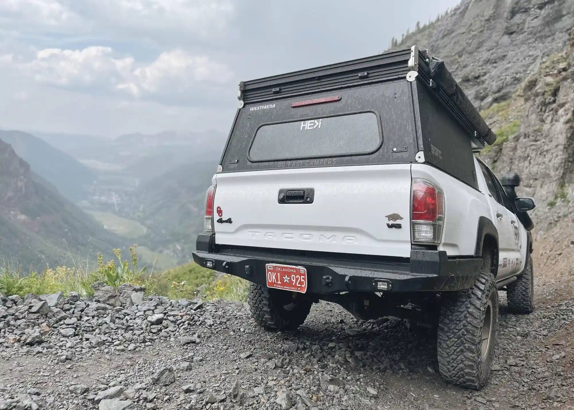 Rear-facing view of a 3rd Gen Toyota Tacoma driving off road in the mountains with a Backwoods Adventure Mods Hi-Lite High Clearance Rear Bumper installed