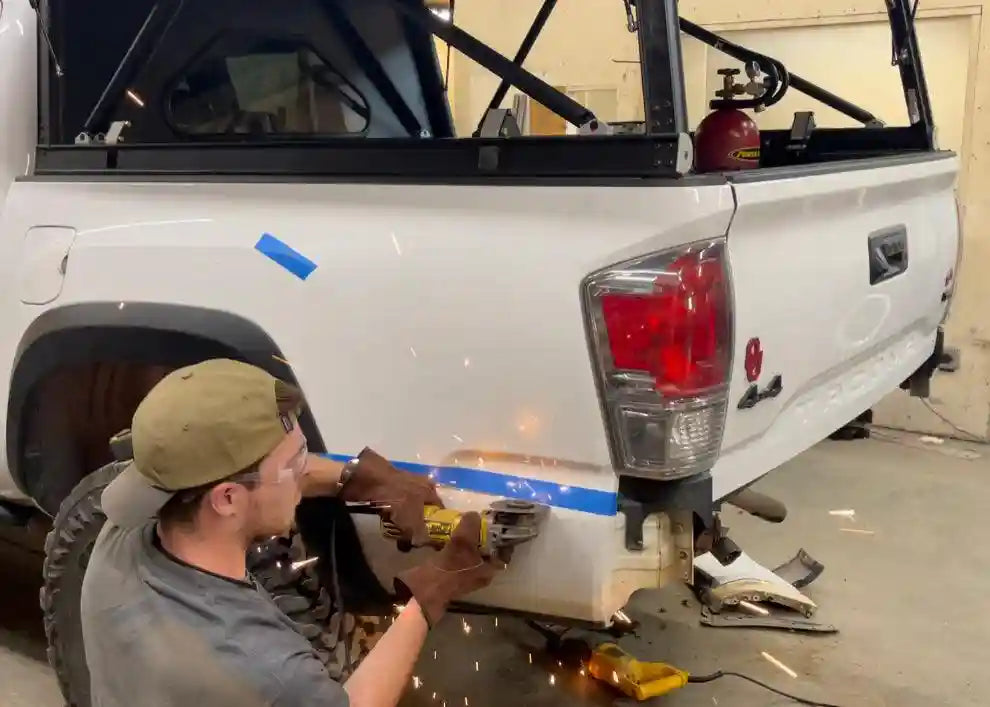 Man performing a DIY installation of the Backwoods Adventure Mods 2016-2023 3rd Gen Toyota Tacoma Hi-Lite High Clearance Rear Bumper