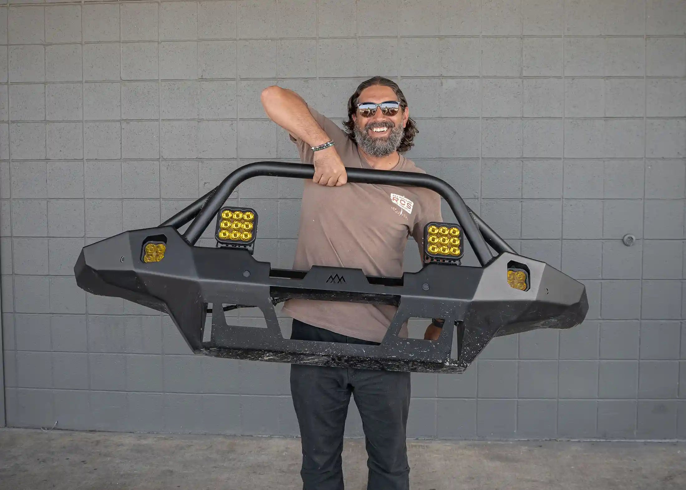 Man lifting the 2024 4th Gen Toyota Tacoma Backwoods Adventure Mods Hi-Lite Overland hybrid aluminum high clearance Front Bumper with Prerunner Bull Bar with one hand