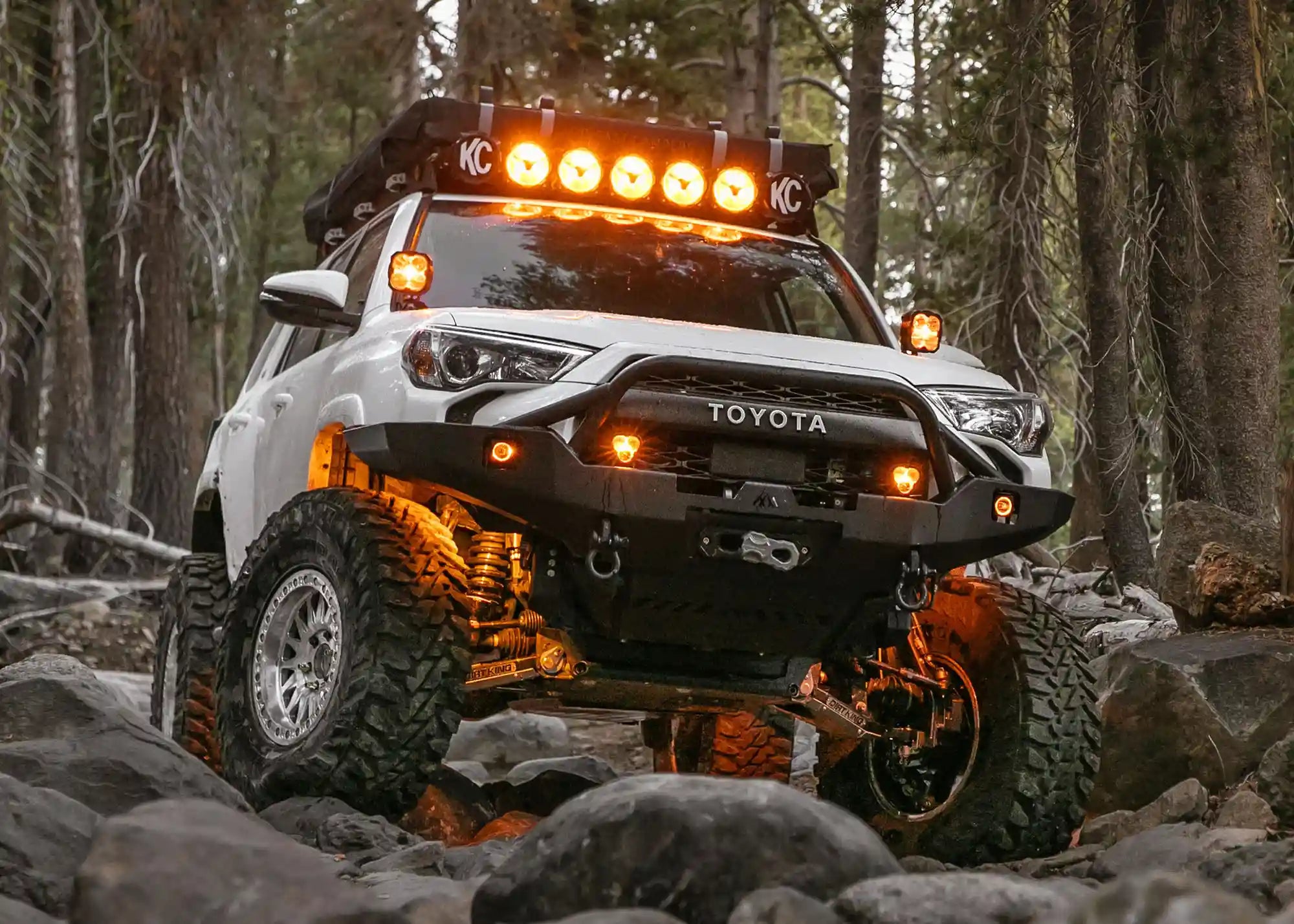 White 5th Gen Toyota 4runner equipped with a Backwoods Adventure Mods Hi-Lite Overland Front Bumper with Prerunner Bull Bar driving off road at night with LED off road lights mounted