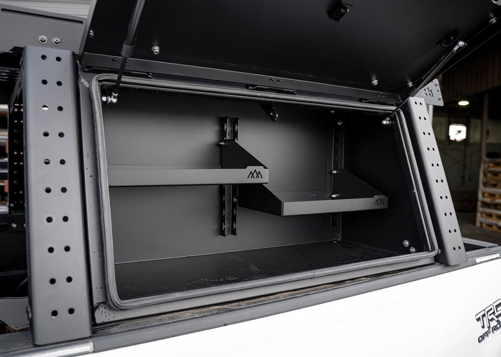 Interior details of the cargo storage box with shelving included in the Backwoods Adventure Mods Tacoma Truck Bed Rack Storage System Bundle
