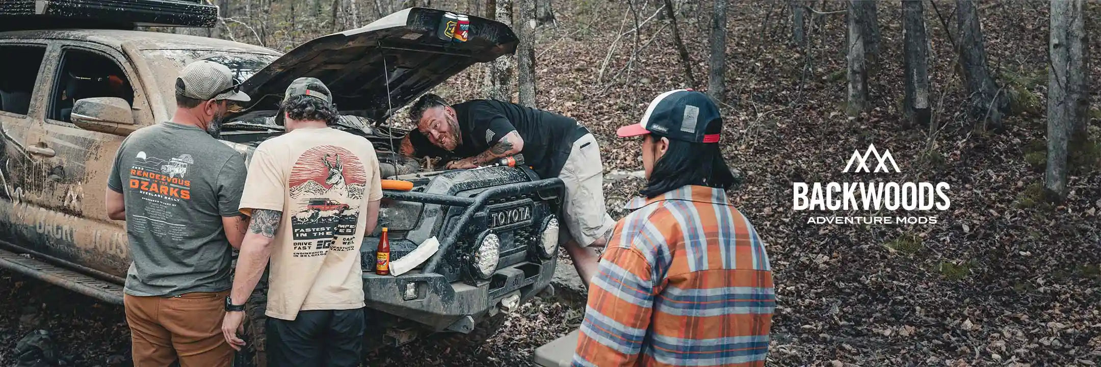 Backwoods Adventure Mods Crew standing around a Toyota Tacoma with the hood open off road working on the engine
