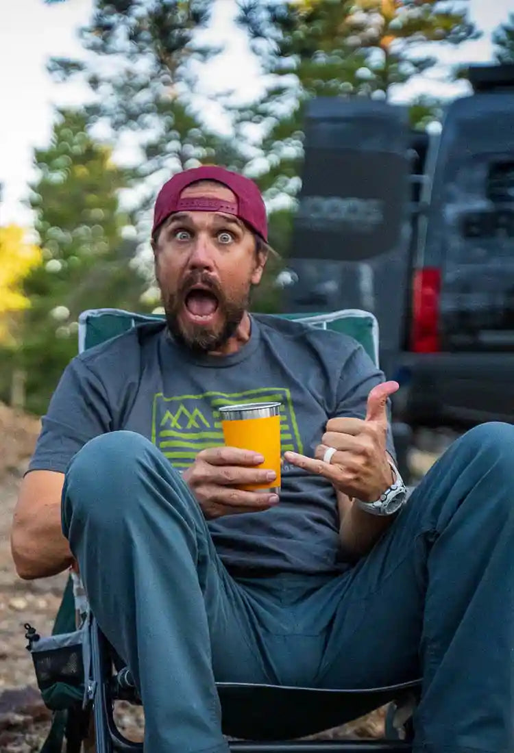Man sitting in a camp chair holding a dring and wearing a Backwoods Adventure Mods t-shirt