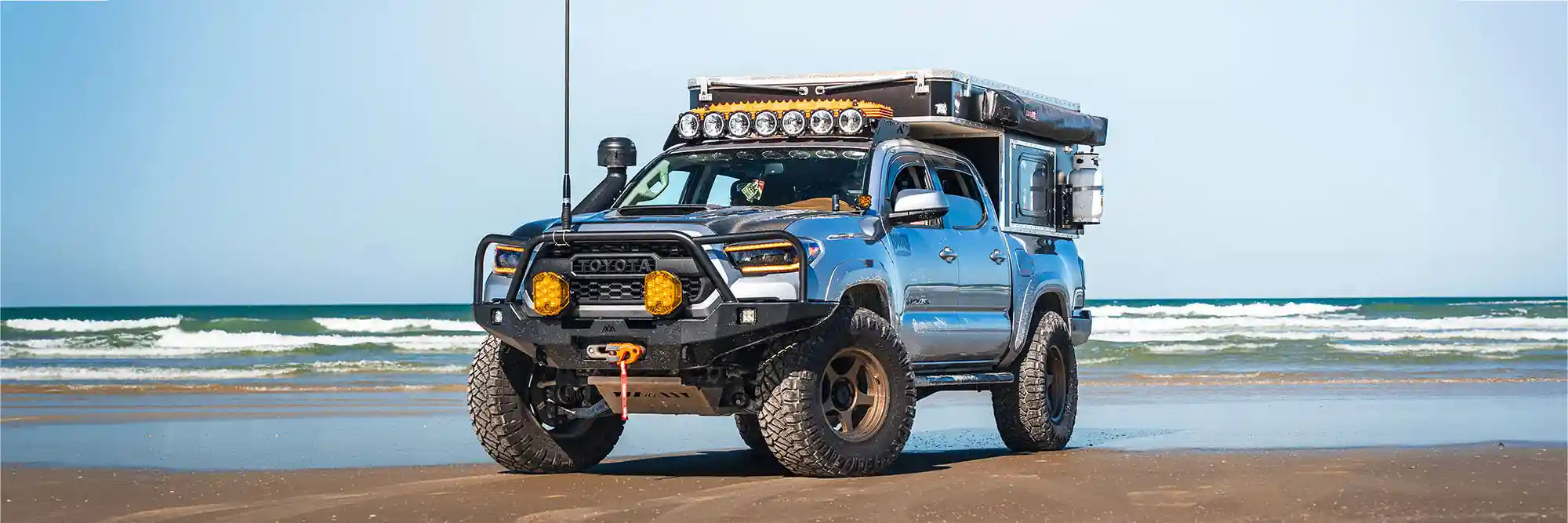 Toyota Tacoma equipped with Backwoods Adventure Mods and accessories parked in front of the ocean on a beach