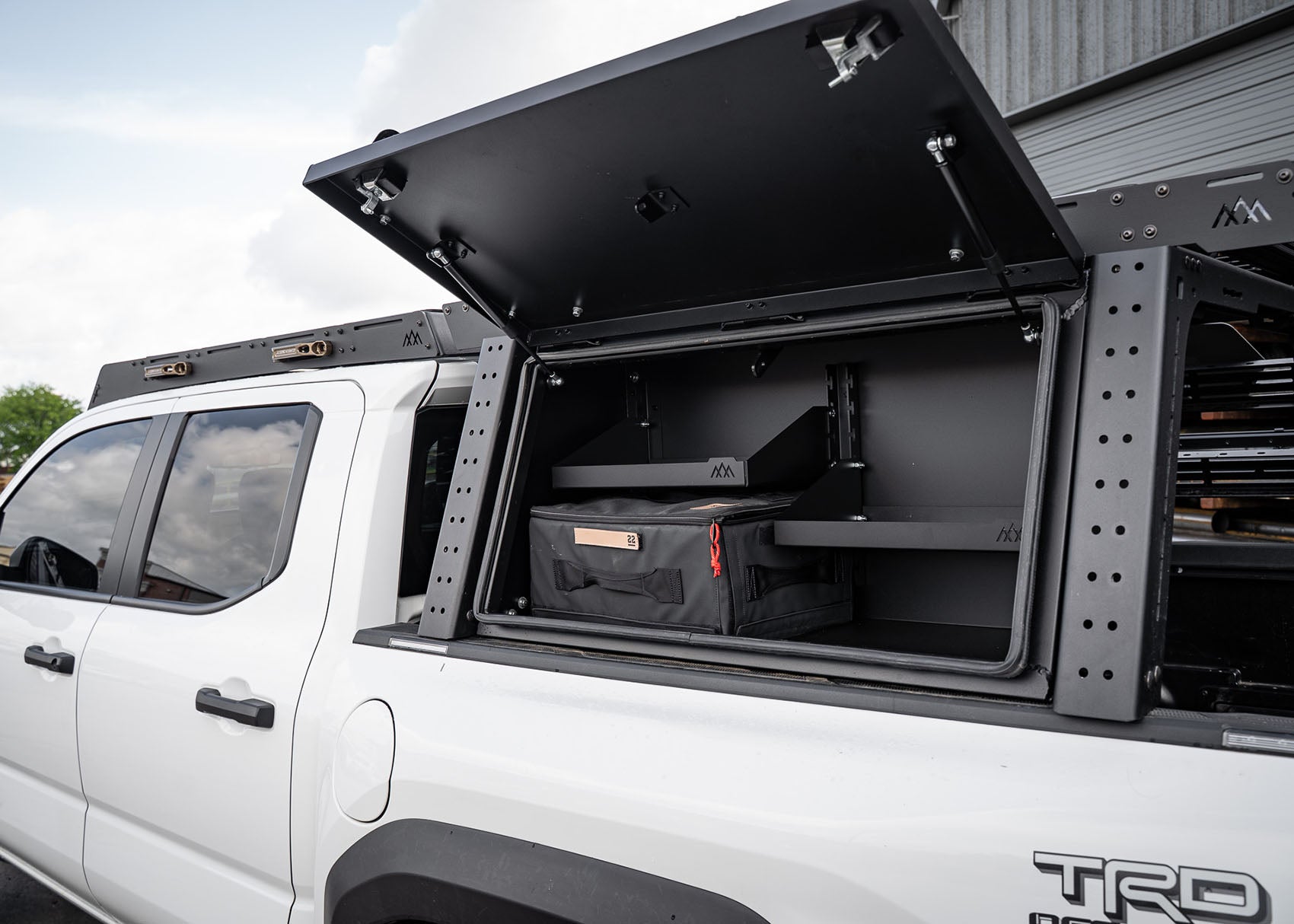 Optional aluminum cargo storage box with locking lid installed on the Backwoods Adventure Mods Toyota Tacoma Overland Truck Bed Rack