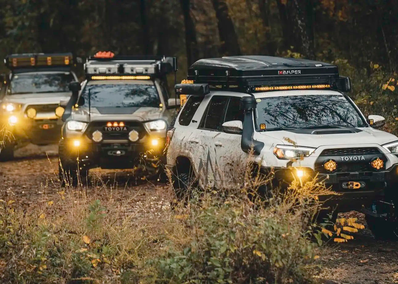 multiple overland vehicles driving at dusk with a variety of off road lights on
