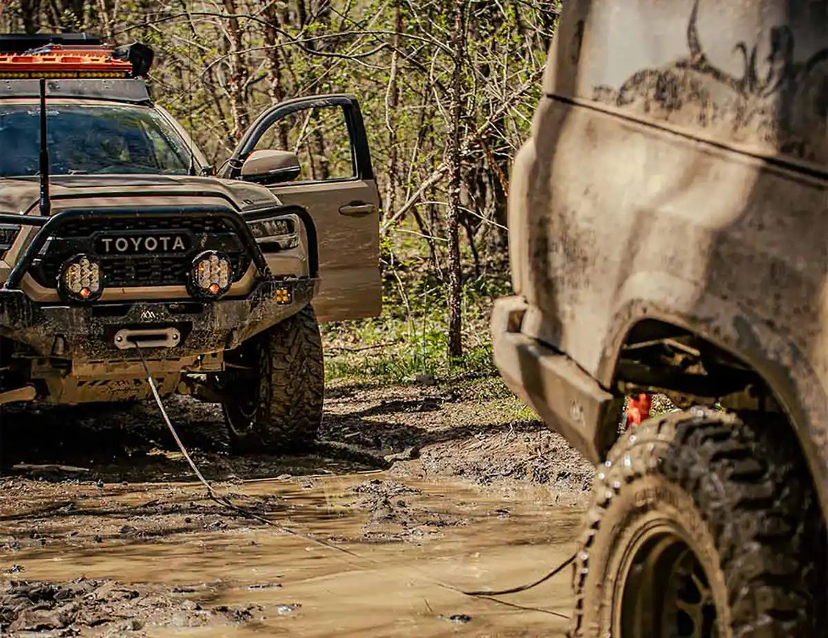 Winch installed on an overland truck being used for an off road recovery to pull a stuck Tacoma from the mud