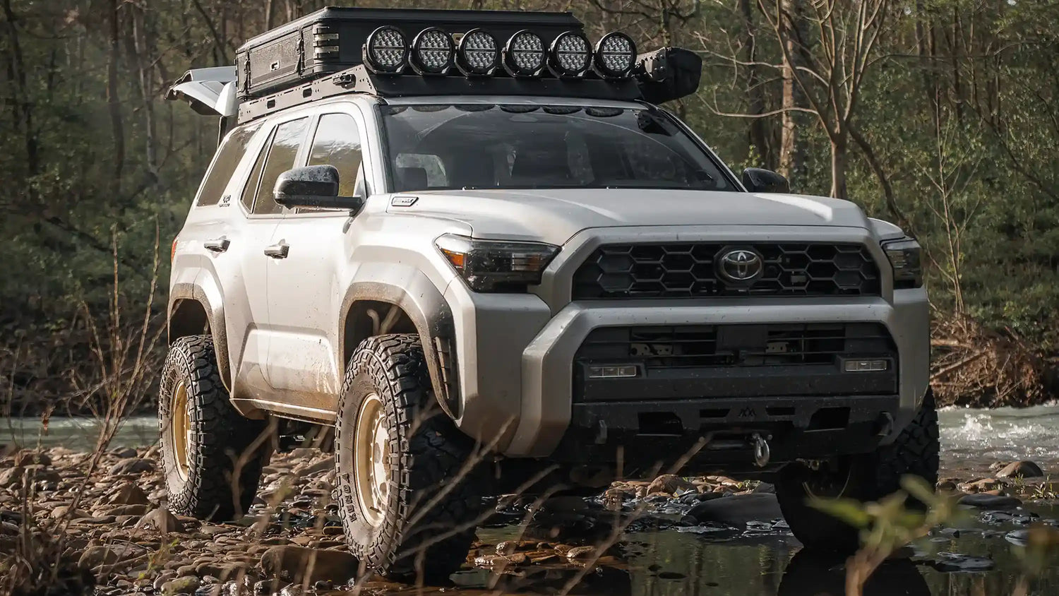 6th Gen Toyota 4Runner driving off road equipped with several mods - including a roof rack, awning, rooftop tent, hidden winch bumper, lights and other overland accessories - from Backwoods Aventure Mods