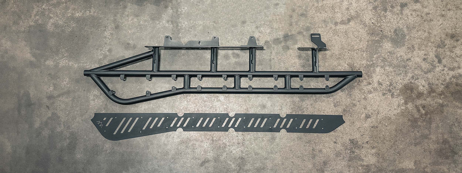 A set of bolt-on Tacoma Rock Sliders from Backwoods Adventure Mods on a floor showing the various components