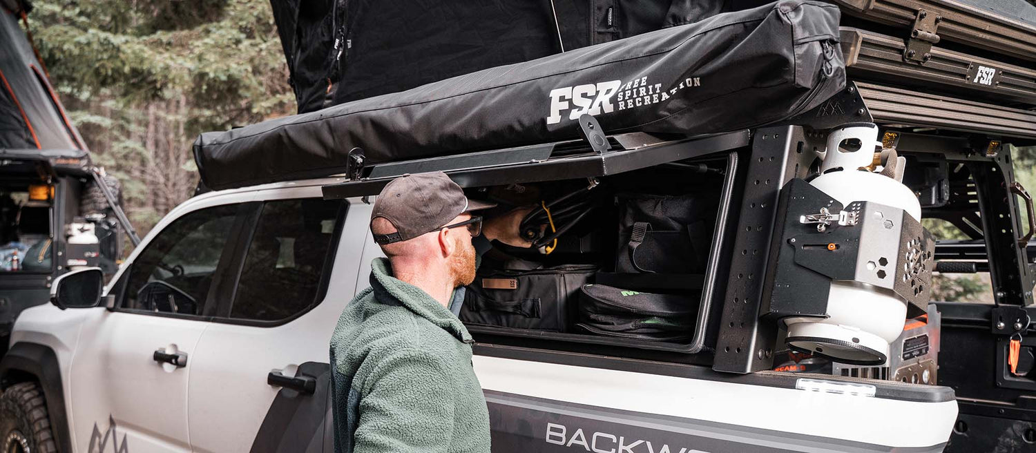 A man using a storage box on the back of a 4g tacoma bed rack from backwoods adventure mods