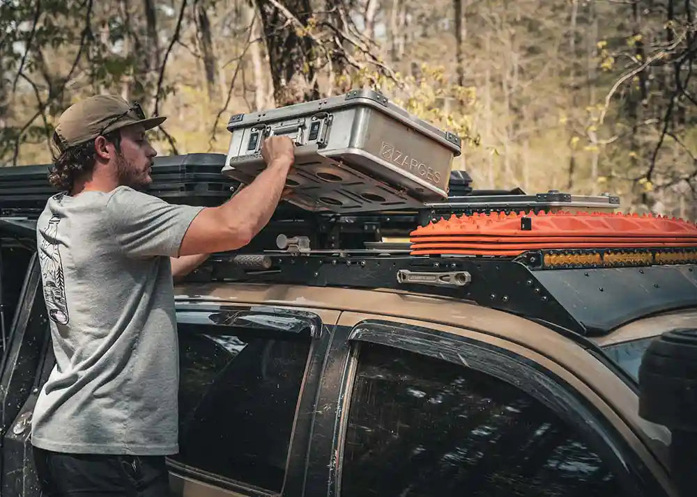 Man securing cargo storage boxes to the roof of his Tacoma using the Backwoods Adventure Mods 2005-2023 2nd and 3rd Gen Toyota Tacoma DRIFTR Roof Rack