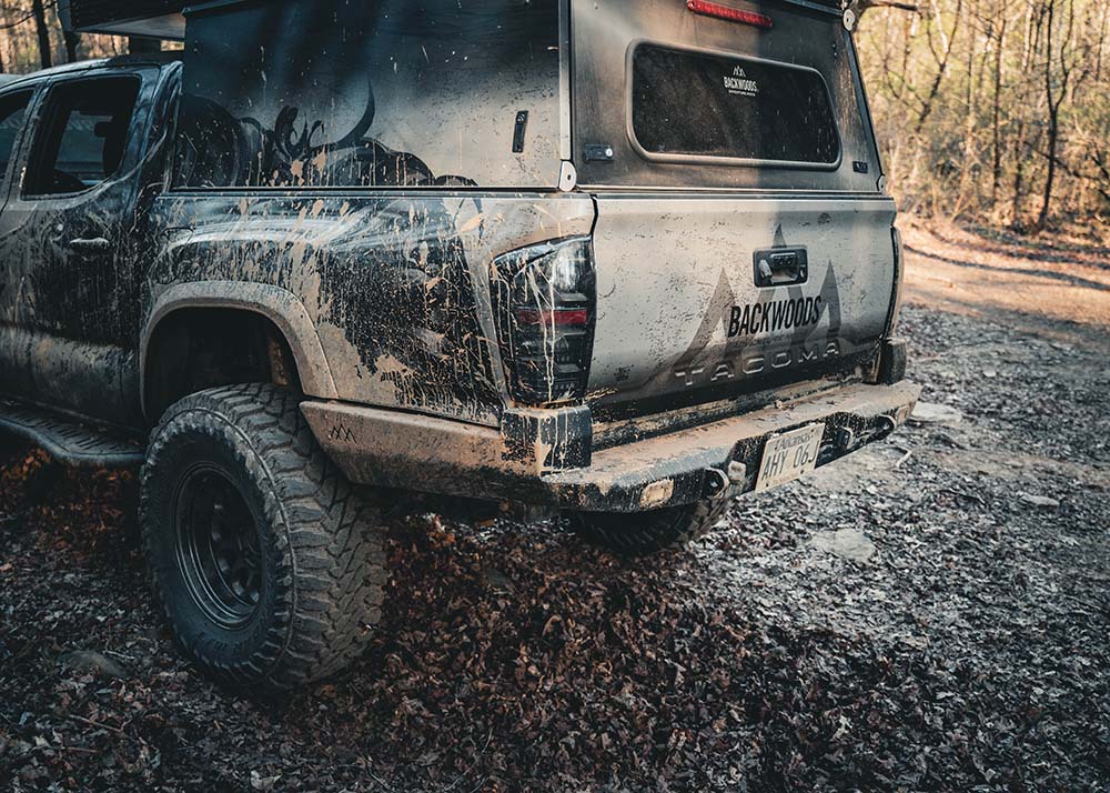 Mud covered Backwoods Adventure Mods Toyota Tacoma (2016-2023) Hi-Lite High Clearance Rear Bumper installed on a black 3rd Gen Tacoma