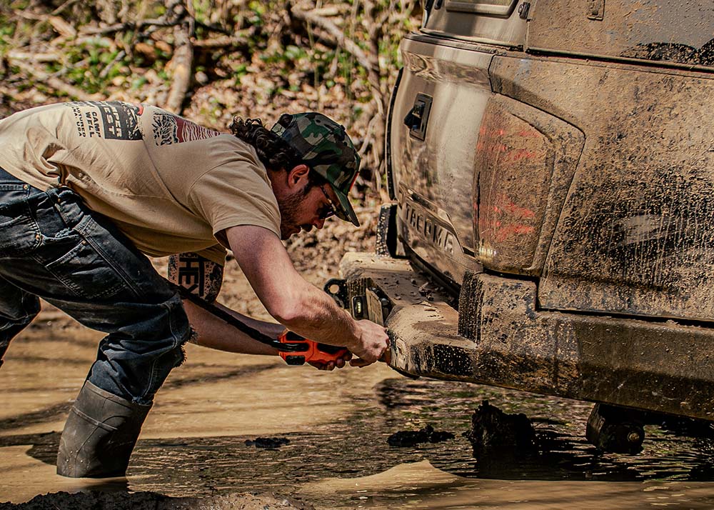 Image of man attaching winch hook to the Backwoods Adventure Mods 2016-2023 3rd Gen Toyota Tacoma Hi-Lite High Clearance Rear Bumper while driving off road