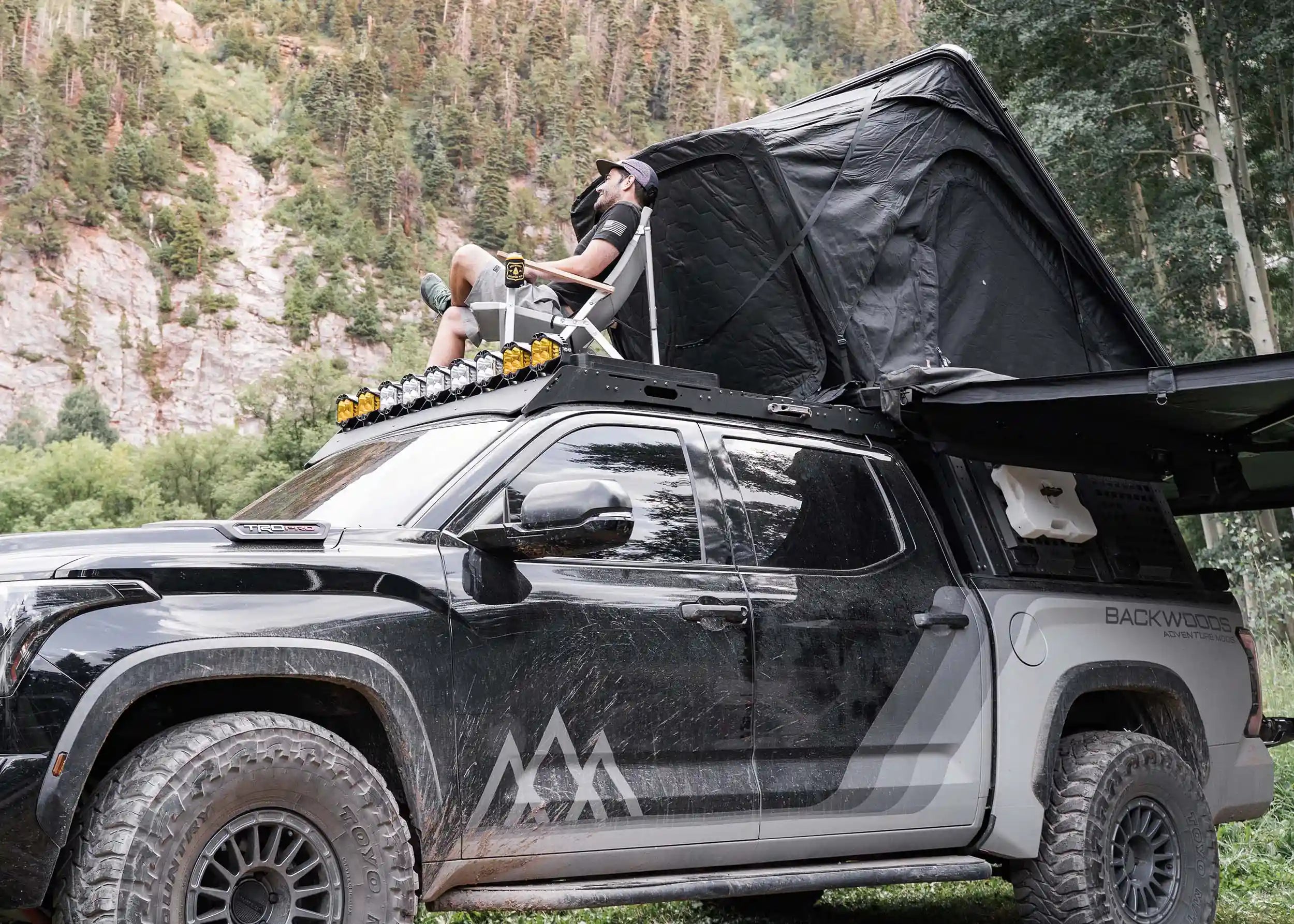 Man relaxing in a camp chair on top of a Backwoods Adventure Mods DRIFTR roof rack installed on a 3rd Gen Toyota Tundra with a roof top tent