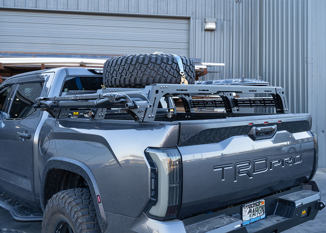 Backwoods Adventure Mods 3rd Gen Toyota Tundra mid-height Bed Rack with off road lights, spare tire, traction boards, and bike tray accessories installed