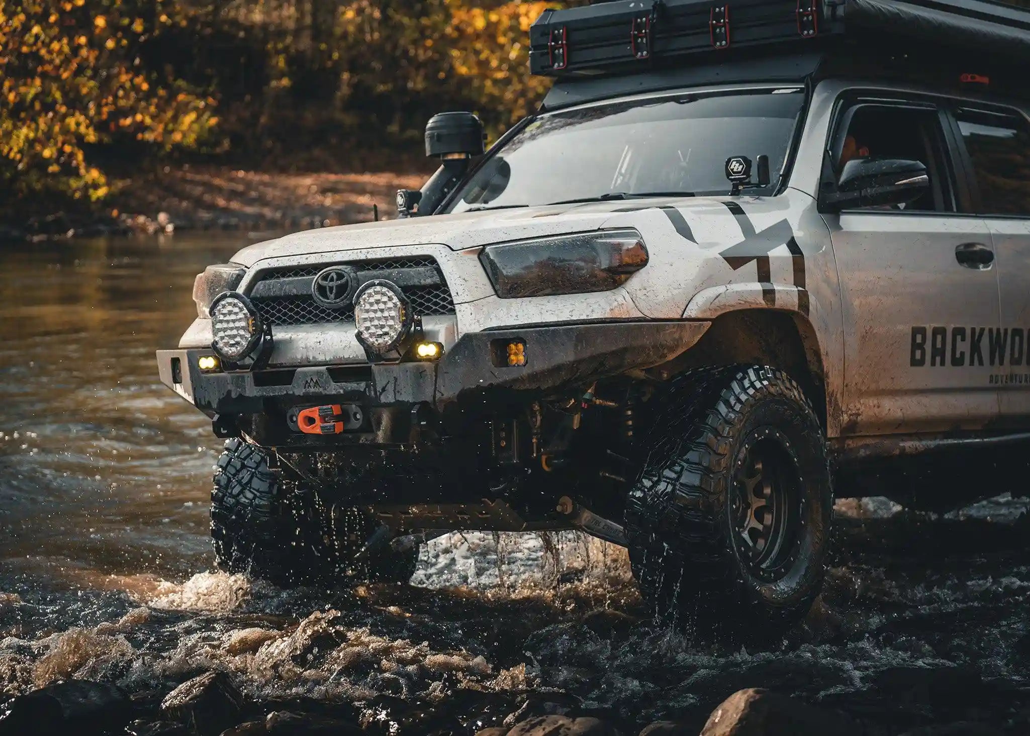 Backwoods Adventure Mods 2014-2022 5th Gen Toyota 4Runner Hi-Lite Overland Off Road Front Bumper installed on a white 4runner with winch installed driving through water off road