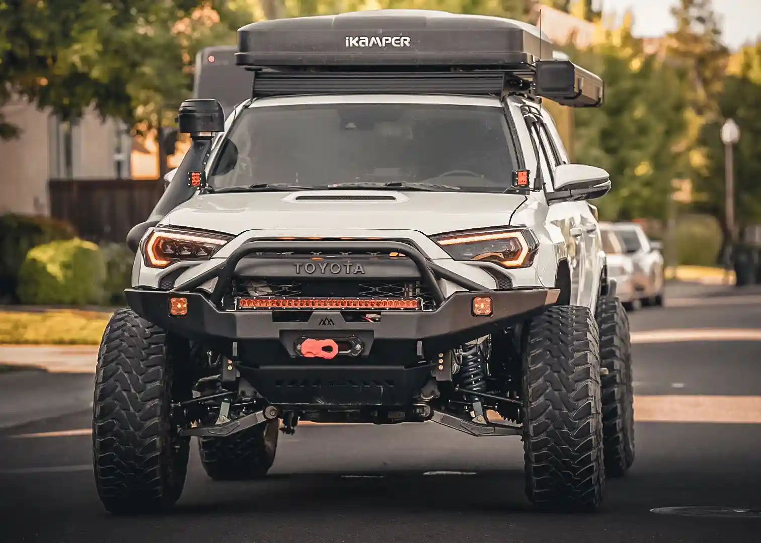 5th Gen Toyota 4runner equipped with a Backwoods Adventure Mods Hi-Lite Overland Front Bumper with Prerunner Bull Bar driving at dusk with winch and LED lights mounted on the bumper