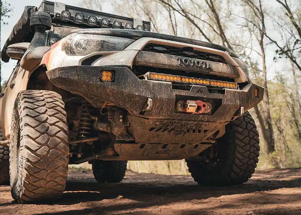 Image of a 5th Gen Toyota 4Runner with Aluminum Connector Skid Plate and Backwoods Adventure Mods Hi-Lite Overland Front Bumper installed and covered in mud while driving off road 