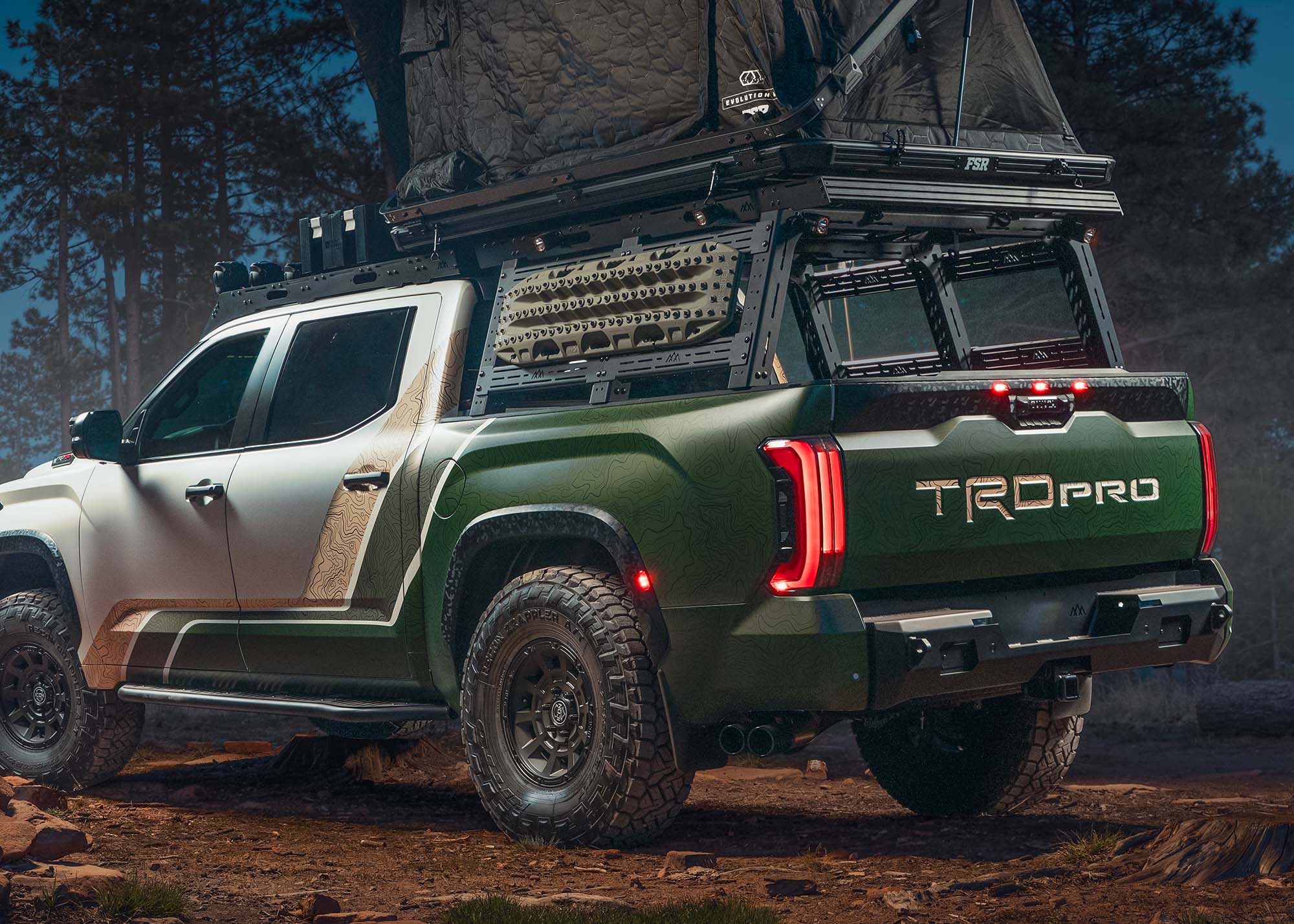 Green and white truck with a roof rack in a forest setting