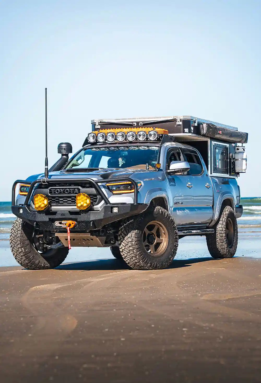 Toyota Tacoma equipped with Backwoods Adventure Mods and accessories parked in front of the ocean on a beach