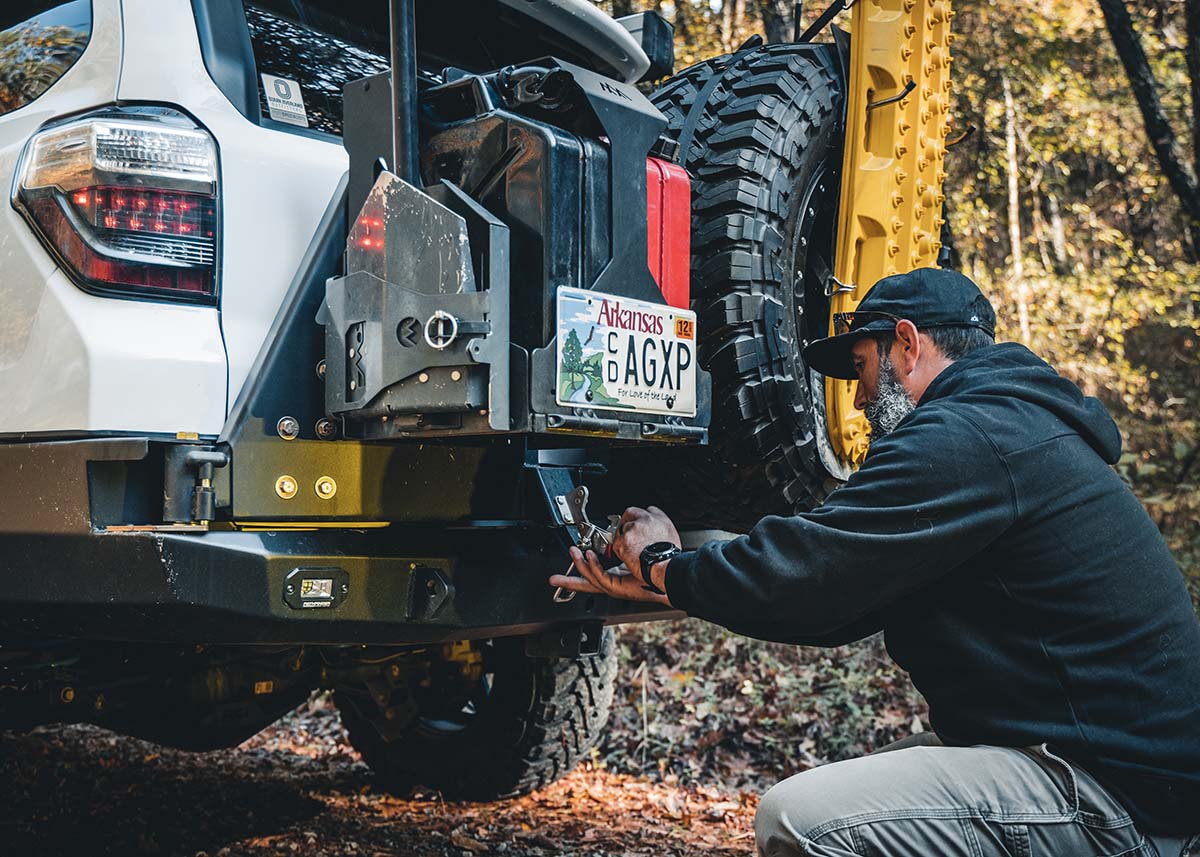 Man using the Backwoods Adventure Mods Jerry Can Holder Mount installed on the bumper of his Toyota 4Runner for off road gear and jerry can storage