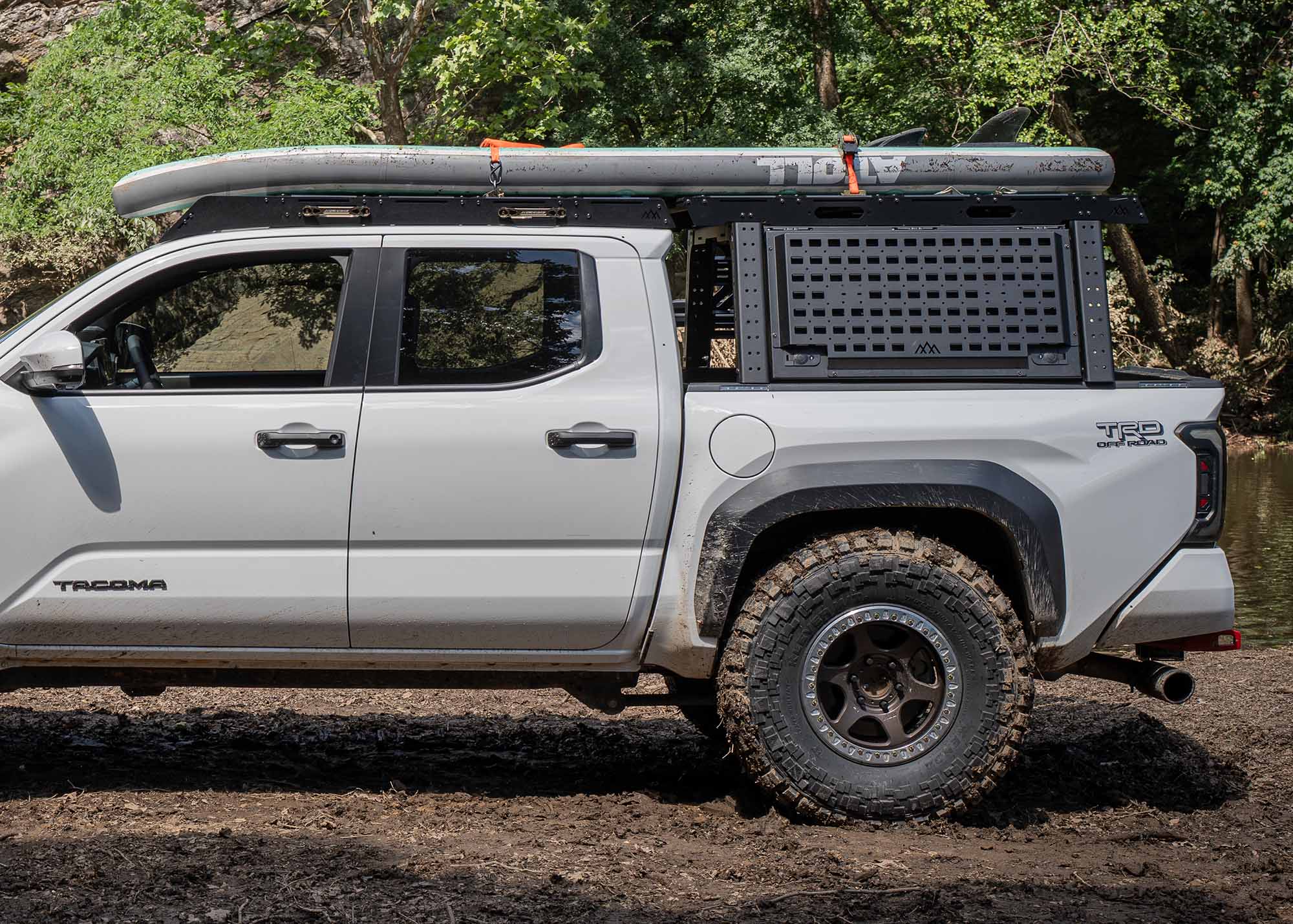 2024 Toyota Tacoma with a Backwoods Adventure Mods Tacoma Overland Bed Rack installed and being used to haul paddleboards with a river in the background