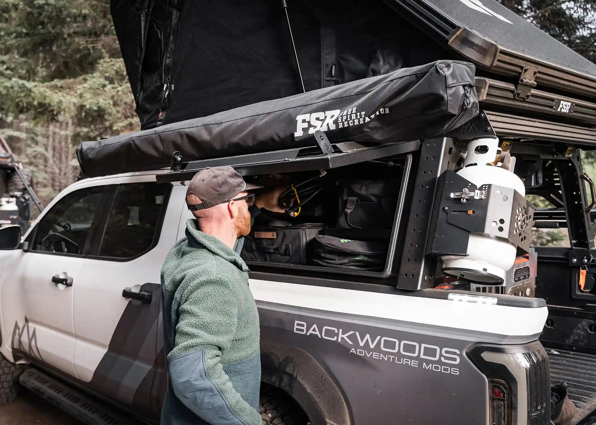 Man removing gear from the Backwoods Adventure Mods Toyota Tacoma bed rack storage box while camping