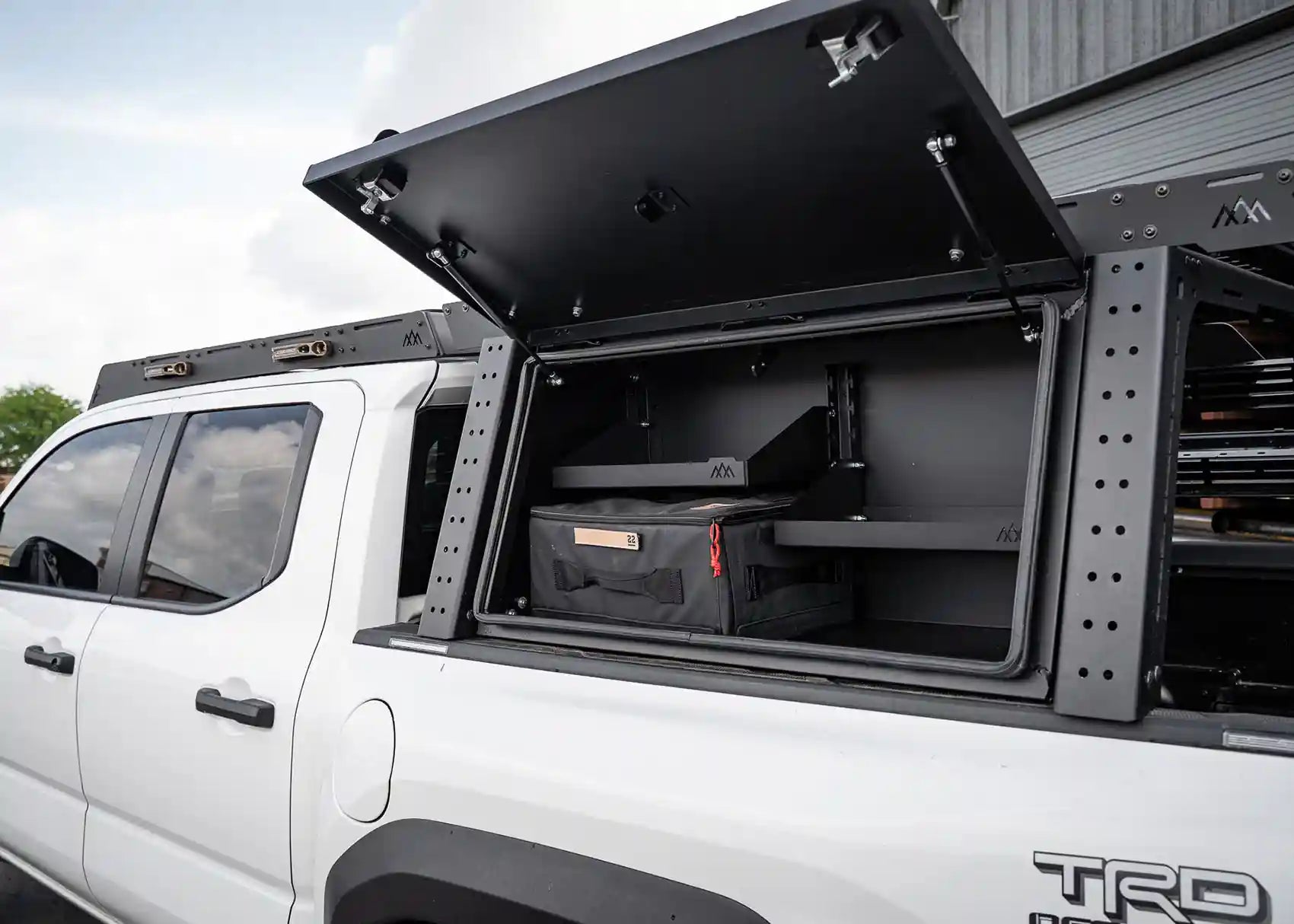 Backwoods Adventure Mods Toyota Tacoma bed rack storage box with lid open showing shelving for organizing off road overlanding gear 